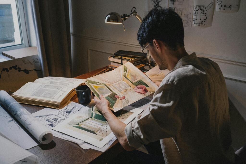 architect-focused-on-interior-design-sketches-at-desk-with-papers-lamp-and-mug-EK908e0v2Jc-4Eb9gIxtEA